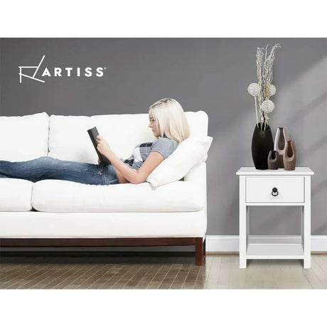 Woman reading on a white sofa next to a white side table with decorative vases.