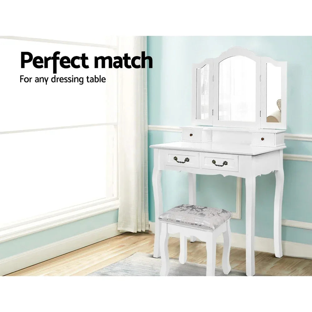 White wooden dressing table with matching cushioned stool in a bright room
