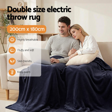 Couple on sofa using laptop, covered by navy double size electric throw rug, 200x180cm.