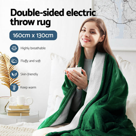 Woman wrapped in green double-sided electric throw rug, holding mug, in cozy living room.