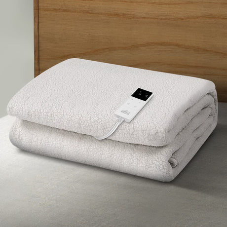 Folded white electric blanket with digital controller on a bed in a modern bedroom setting