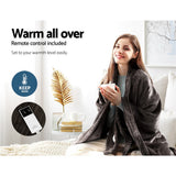 Woman using heated throw rug with remote control, sitting on couch, holding a cup