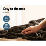 Hand touching a soft, breathable, dark throw rug on a bed in a cozy indoor setting.