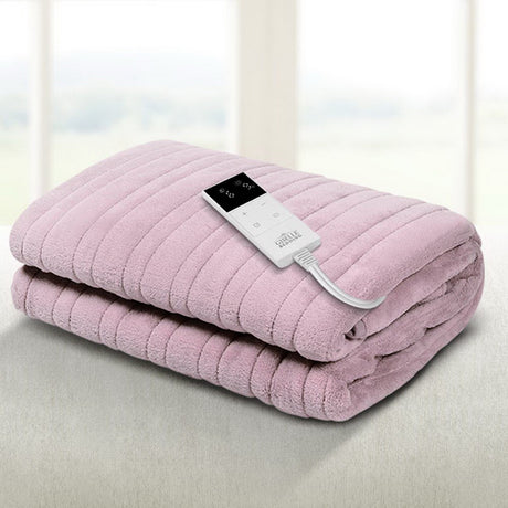 Folded pink electric blanket with remote control on a bed near a window