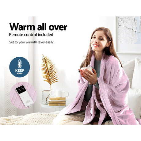 Woman using a pink heated throw blanket with remote control, sitting on a couch.
