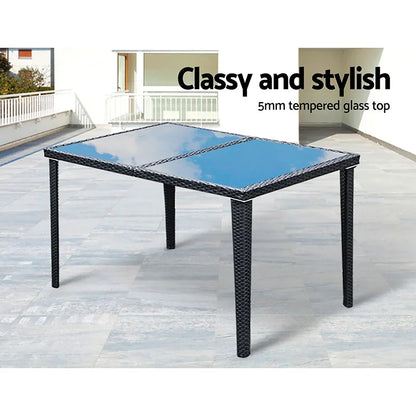Outdoor dining table with black rattan frame and 5mm tempered glass top on patio