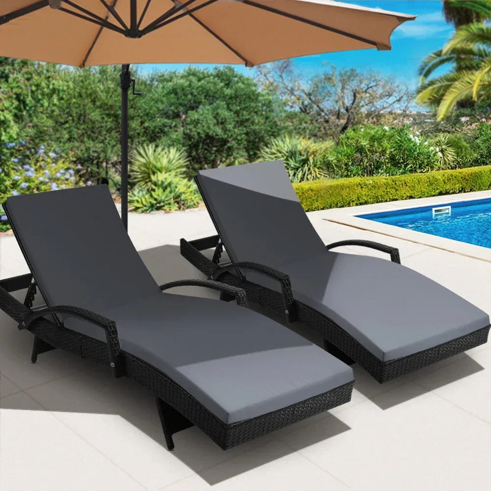 Pair of outdoor rattan lounge chairs with grey cushions by a swimming pool under an umbrella