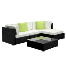 Modern outdoor black wicker lounge set with white cushions, green pillows, and glass table