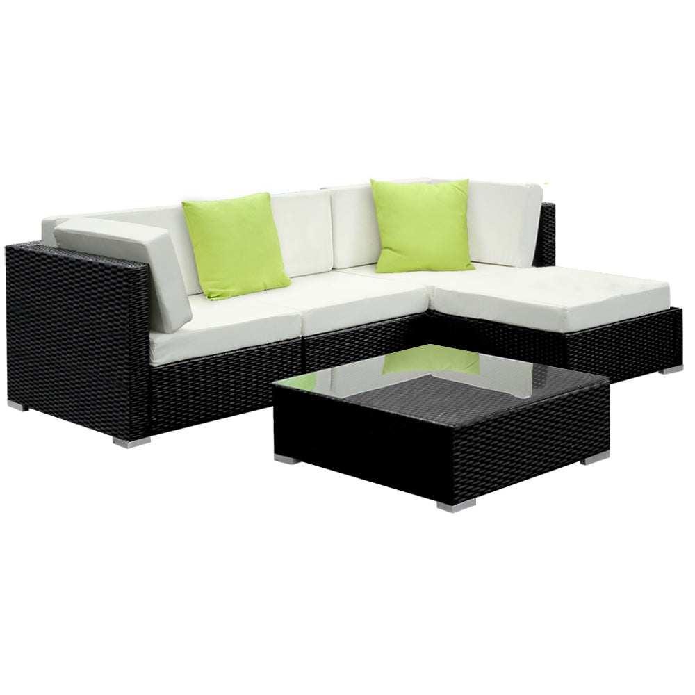 Outdoor rattan sofa set with cream cushions, green accent pillows, and glass coffee table