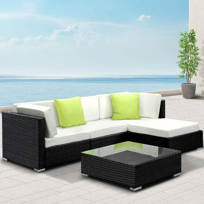 Outdoor black rattan sectional sofa set with white cushions, lime green pillows, and glass coffee table on patio overlooking the ocean.