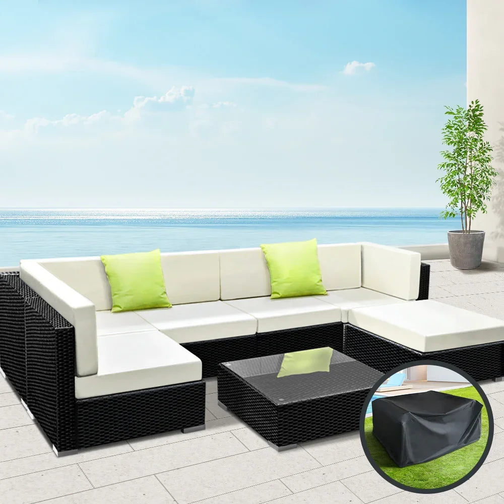 Outdoor black wicker 7-piece modular sofa set with cream cushions, glass coffee table, and green accent pillows on a patio overlooking the ocean.