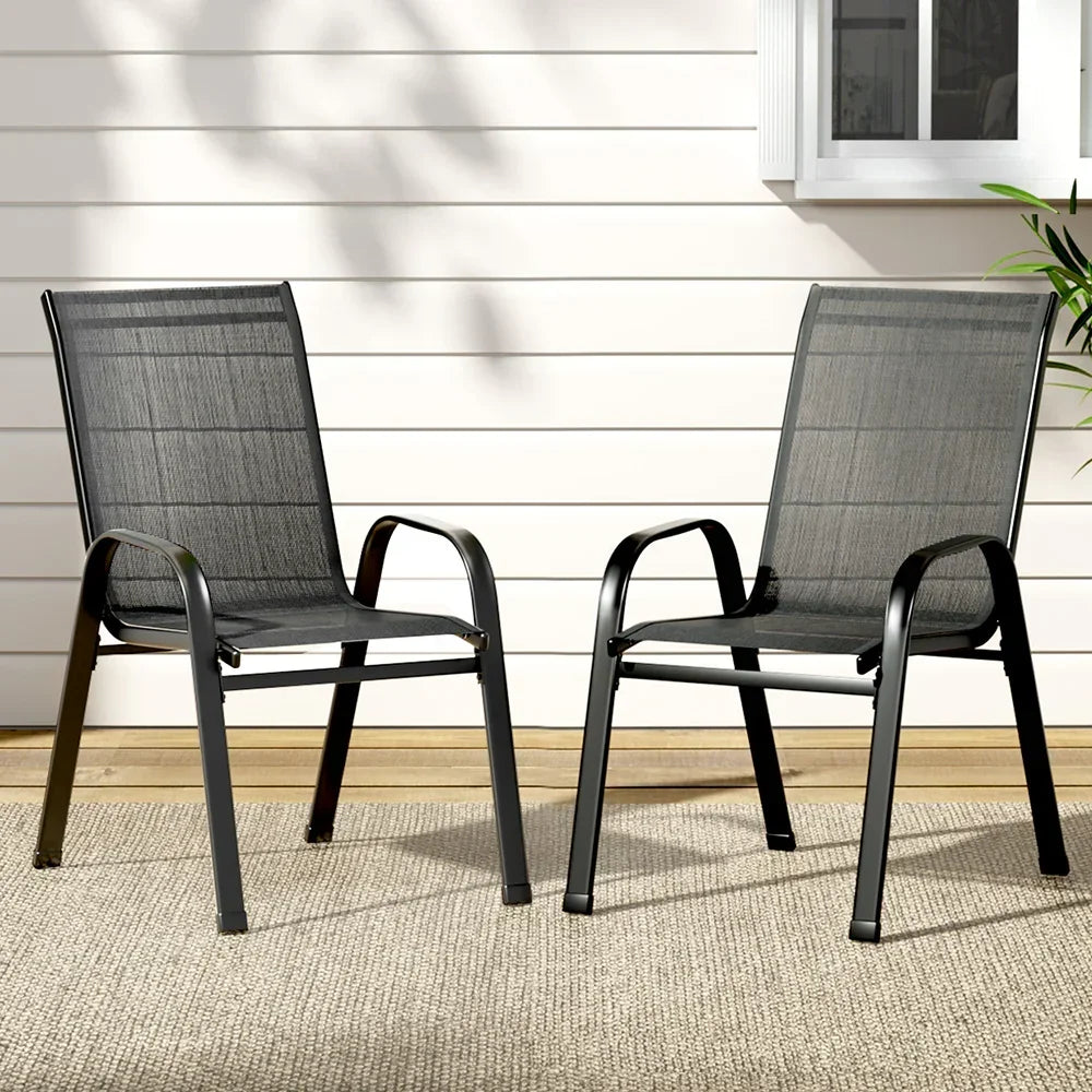 Pair of black outdoor mesh chairs on patio with light wall and window in background