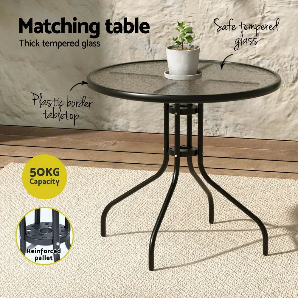 Round outdoor dining table with black metal frame, tempered glass top, and potted plant