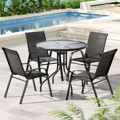 Black outdoor dining set with glass table and four chairs by a pool on tiled patio