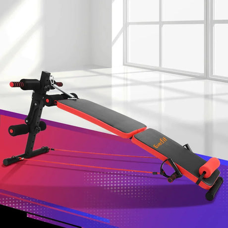 Adjustable sit-up bench with black and red padding, resistance bands, in home gym setting