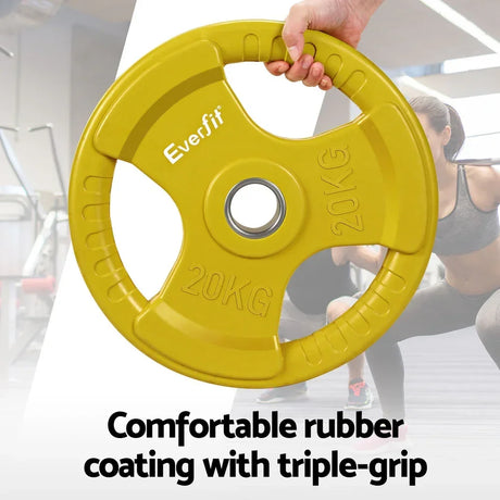 Yellow 20kg rubber weight plate with triple-grip design held in a gym setting