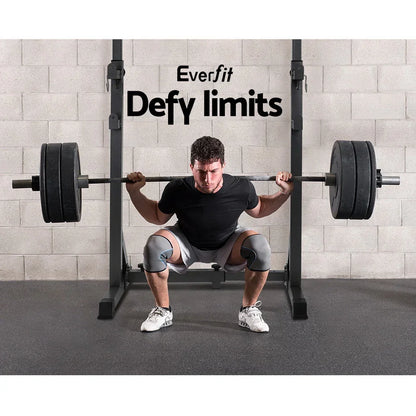 Man performing barbell squat on squat rack in gym with knee sleeves and weight plates
