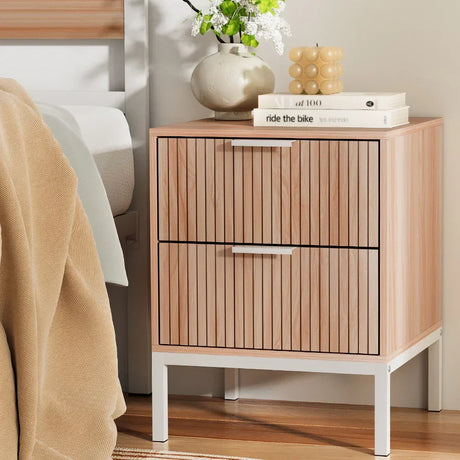 Modern wood bedside table with vertical slat drawers, white legs, and decorative accents