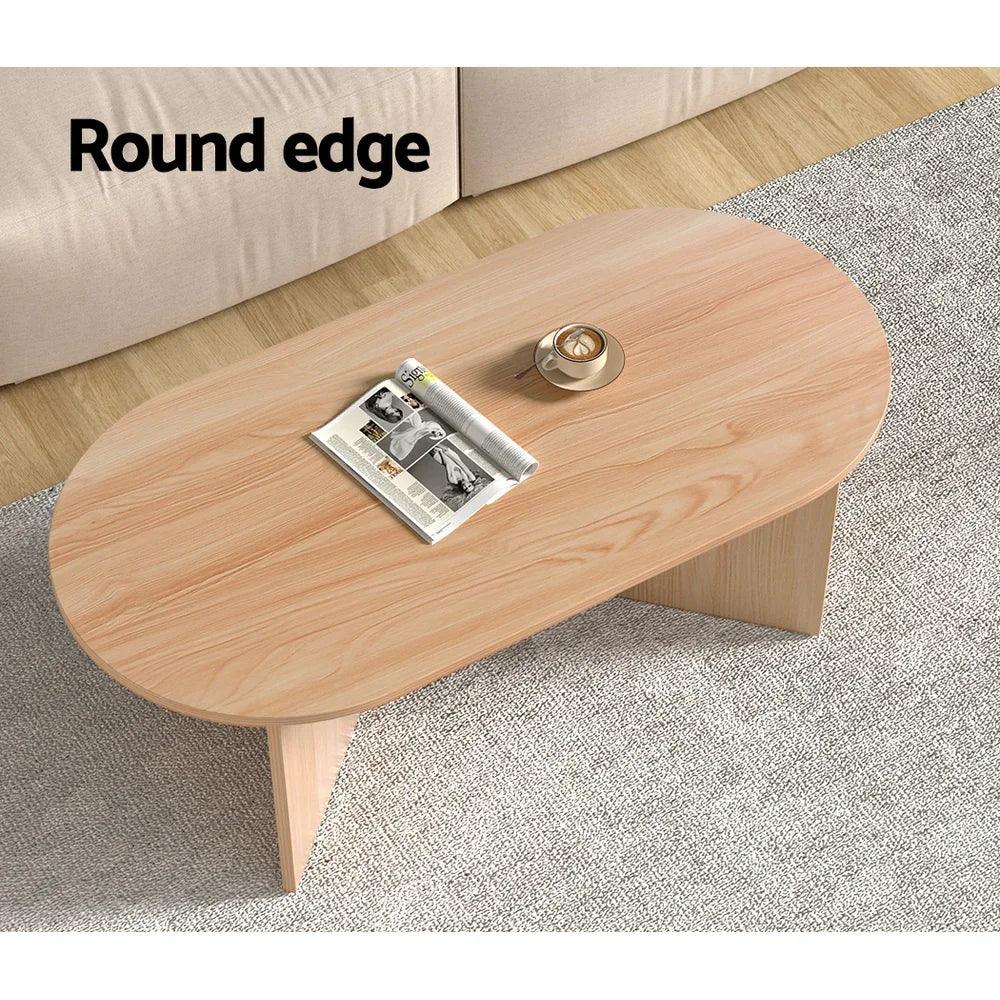 Oval wooden coffee table with round edges, placed on a grey rug in a living room