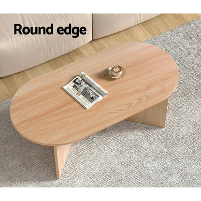 Oval wooden coffee table with round edges, placed on a grey rug in a living room