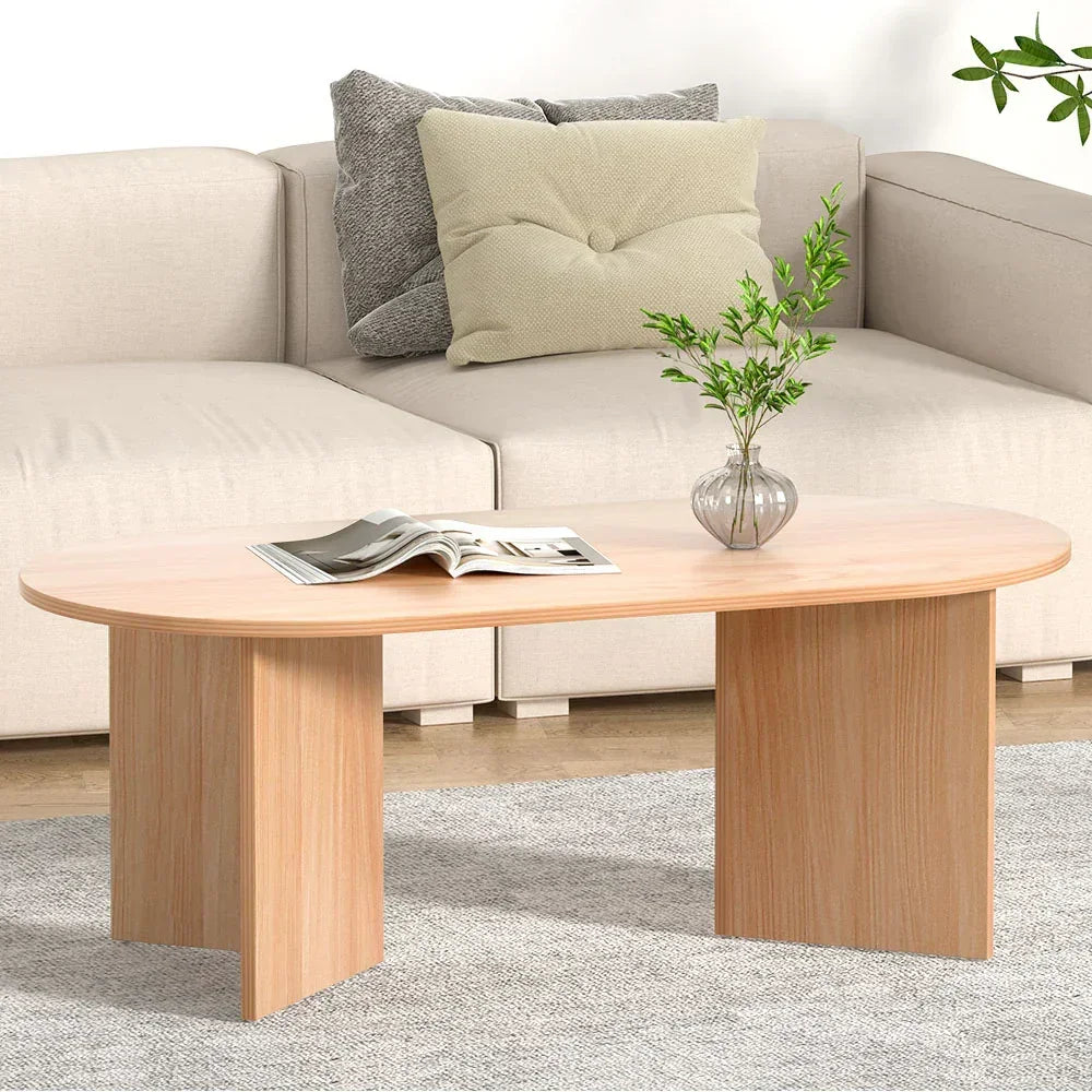 Modern wooden coffee table with oval top, magazine, and glass vase in a living room setting
