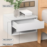 Wall-mounted white bedside table with open drawer, books, vase, and weight capacity labels.