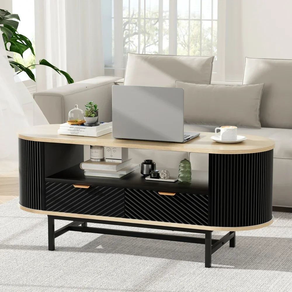 Modern oval coffee table with black and wood finish, open storage, laptop, and decor in living room