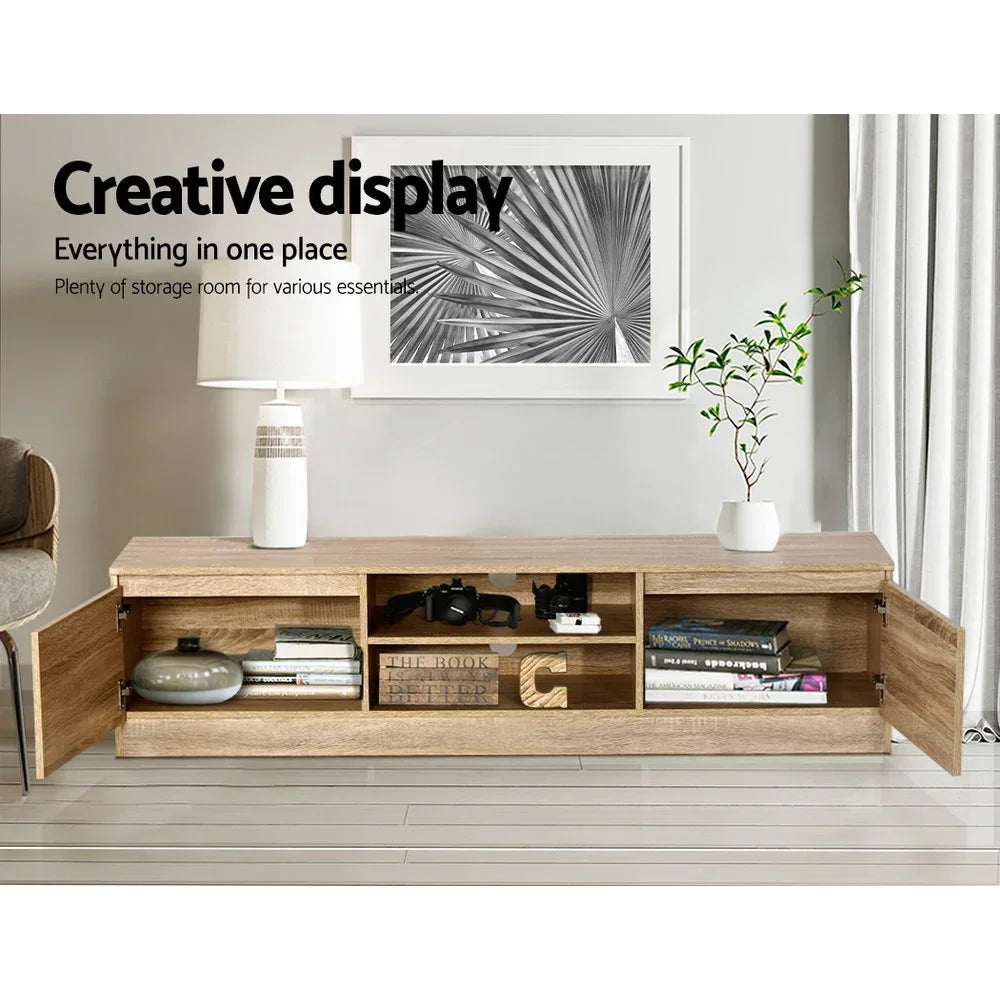 Modern wooden TV unit with open storage shelves, decorative items, books, lamp, and plant in living room