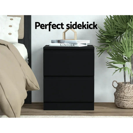 Modern black bedside table with two drawers, books, and decor beside bed and indoor plant