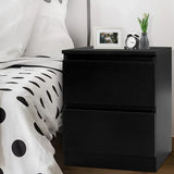 Black bedside table with two drawers beside a bed, topped with a vase, photo frame, and alarm clock
