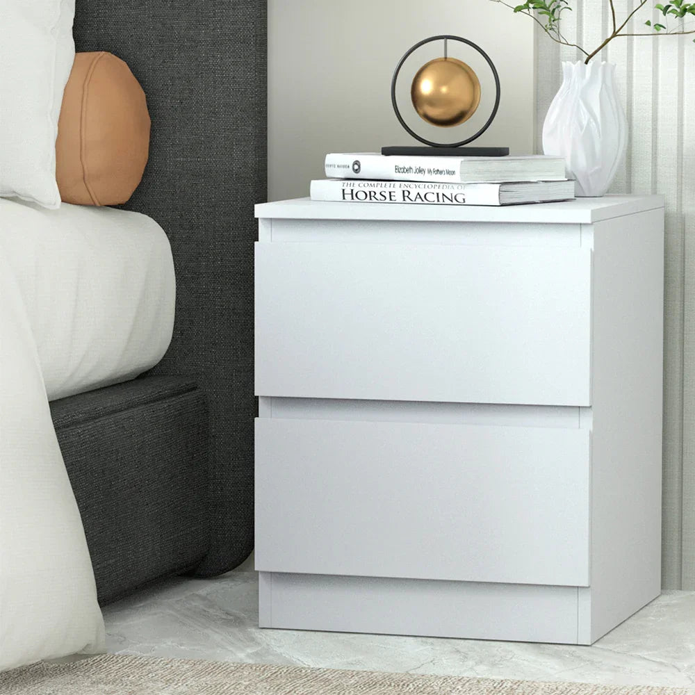 Modern white bedside table with two drawers, books, a decorative sculpture, and a vase