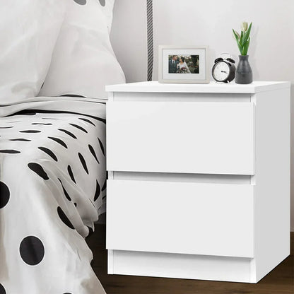 Modern white bedside table with two drawers, beside polka dot bed, decor on top