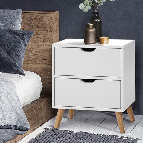 Modern white bedside table with two drawers, wooden legs, styled in a bedroom setting