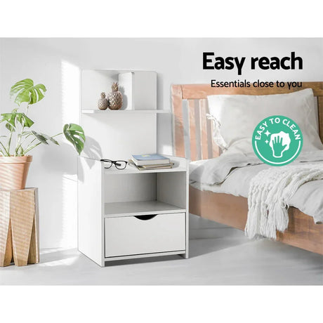 White bedside table with drawer and open shelves beside bed, easy to clean label visible
