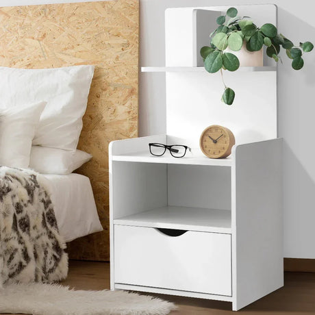 Modern white bedside table with drawer, shelf, clock, glasses, and potted plant in a bedroom