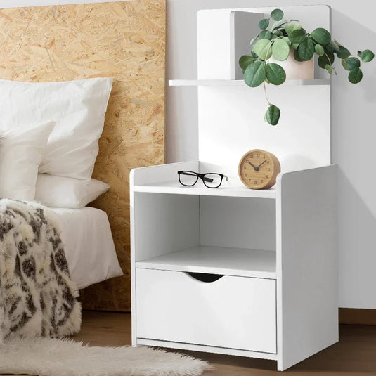 Modern white bedside table with drawer, shelf, clock, glasses, and potted plant in a bedroom