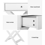 White side table with silver round knob, metal runners, and crossed legs.