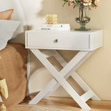 Modern white bedside table with drawer and crossed legs, styled with books and flowers