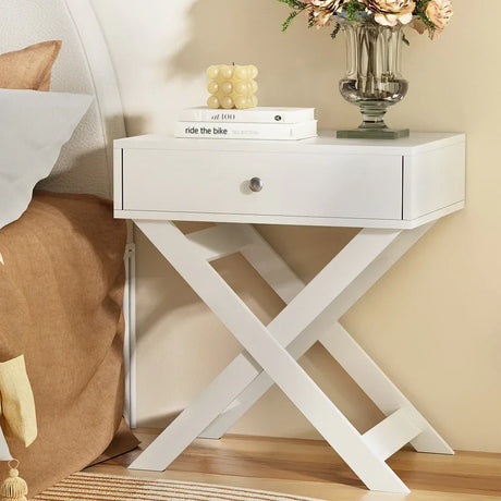 Modern white bedside table with drawer and crossed legs, styled with books and flowers