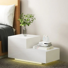 Modern white bedside table with LED lighting, alarm clock, vase, and books in a bedroom setting