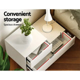 White bedside table with two spacious drawers, lamp, plant and drawer dimensions shown.