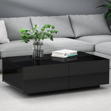 Modern black coffee table with glass top in front of a grey sofa, decorated with plant and books.