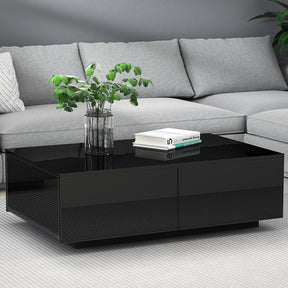 Modern black coffee table with glass top in front of a grey sofa, decorated with plant and books.