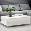 Modern white gloss coffee table in living room with grey sofa, books, and plant decor