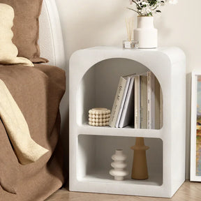 Modern white nightstand with open shelves, vases, books, and minimalist decor beside bed