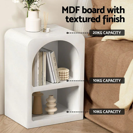 White MDF board bedside table with textured finish, books, and decor items in a modern bedroom.