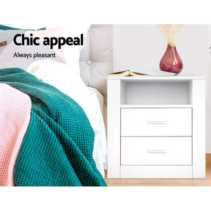 White side shelf nightstand with two drawers, next to bed with teal blanket, book, and vase