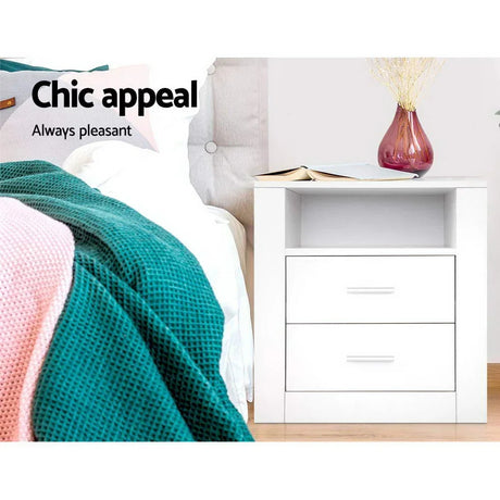 White side shelf nightstand with two drawers, next to bed with teal blanket, book, and vase