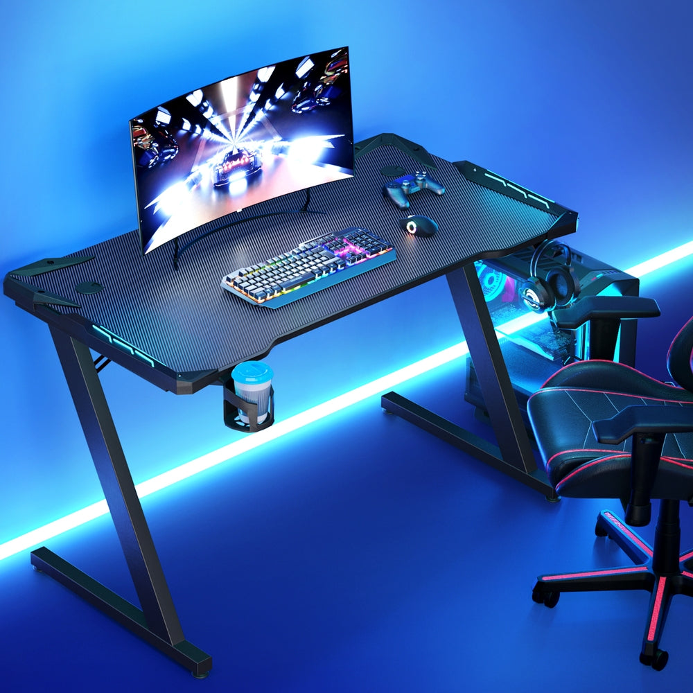 Gaming desk with RGB keyboard, curved monitor, and LED lighting for immersive setup