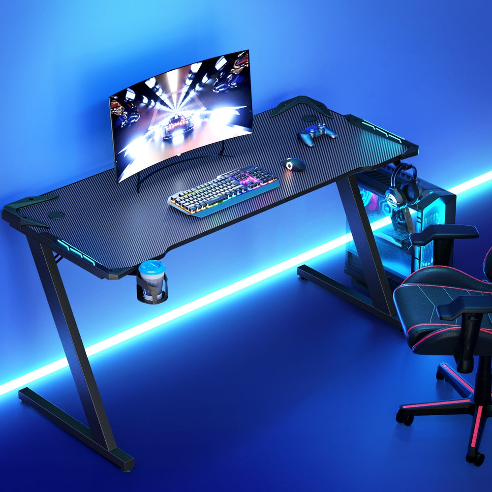 Gaming desk with RGB keyboard, curved monitor, and LED lighting for immersive setup